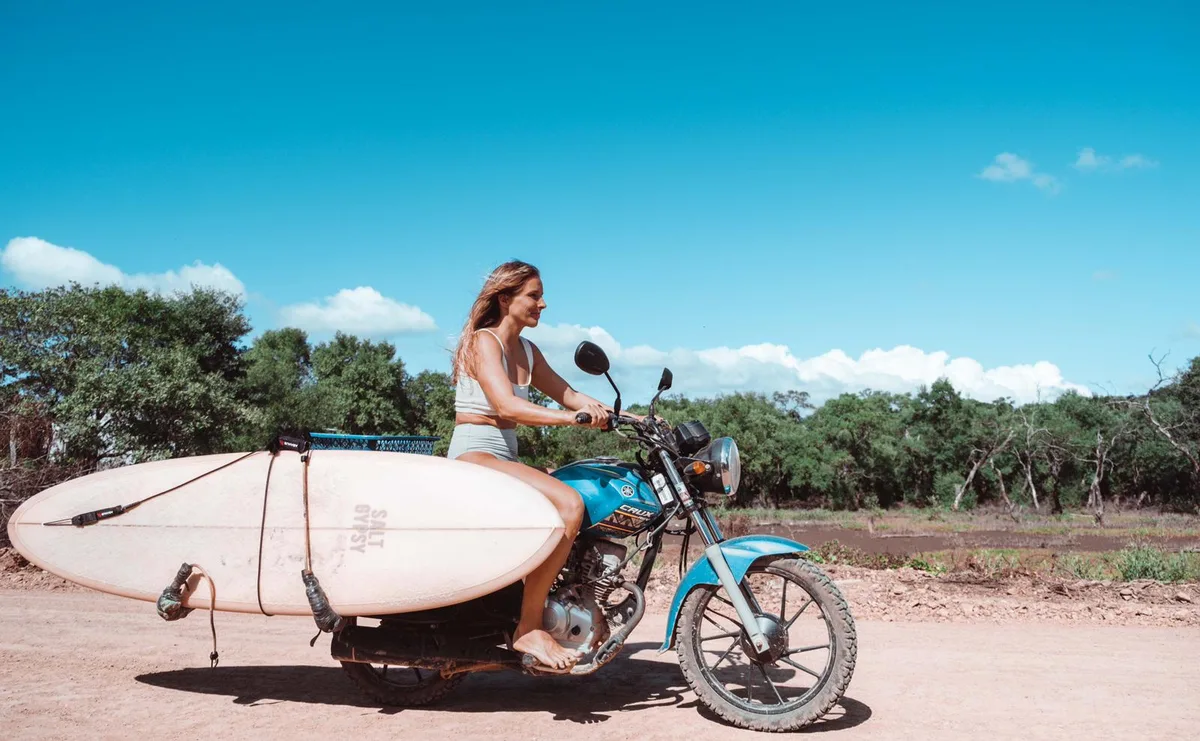 A surfer rides to the break with her board on a motorbike near Waves & Wifi in Popoyo, Nicaragua