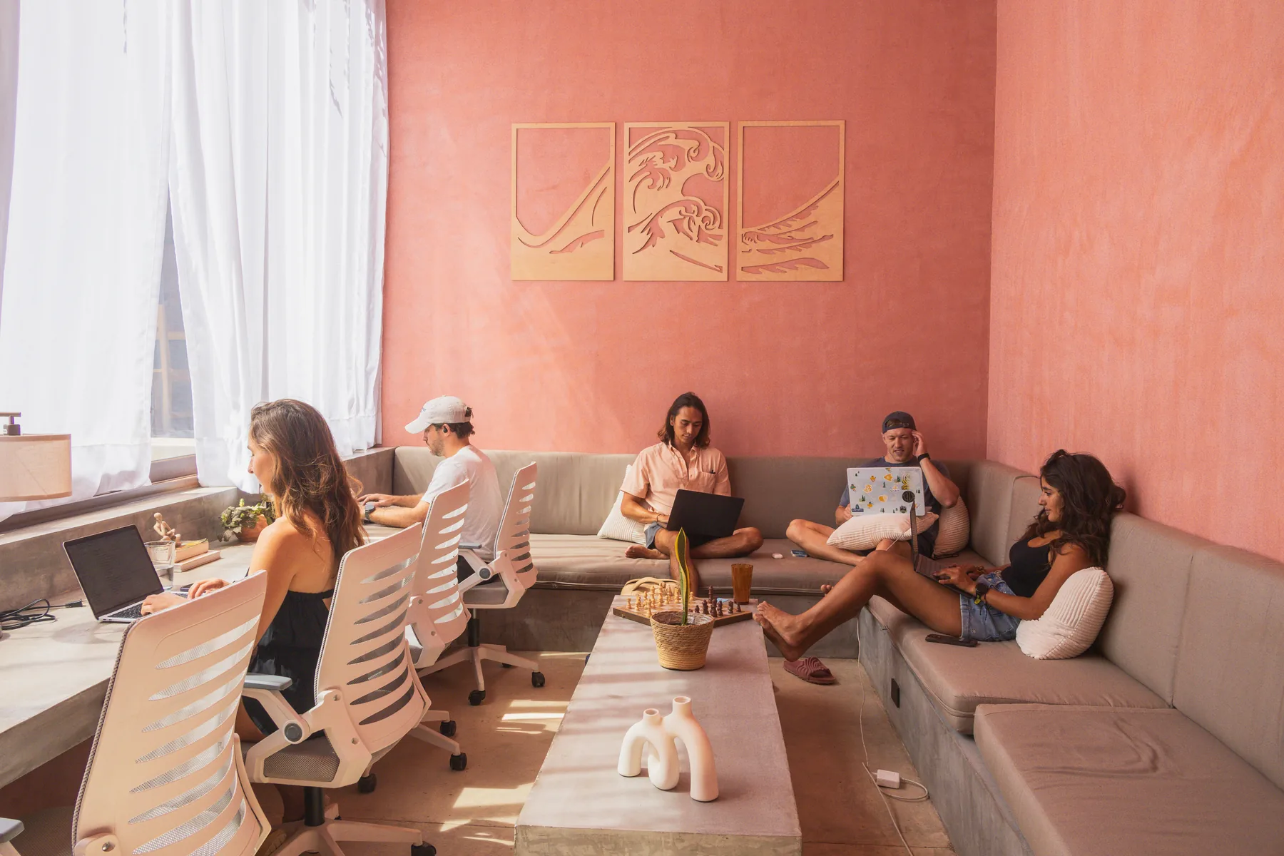 Guests working on laptops together in the coworking lounge under the wave art at Amplitude Coliving, La Punta