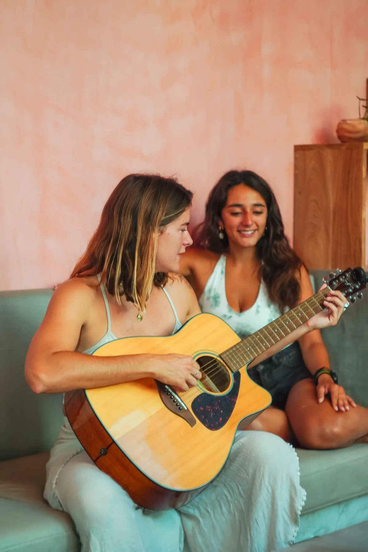 Two guests hanging out on a couch, one playing guitar, in the lounge at Amplitude Coliving, La Punta