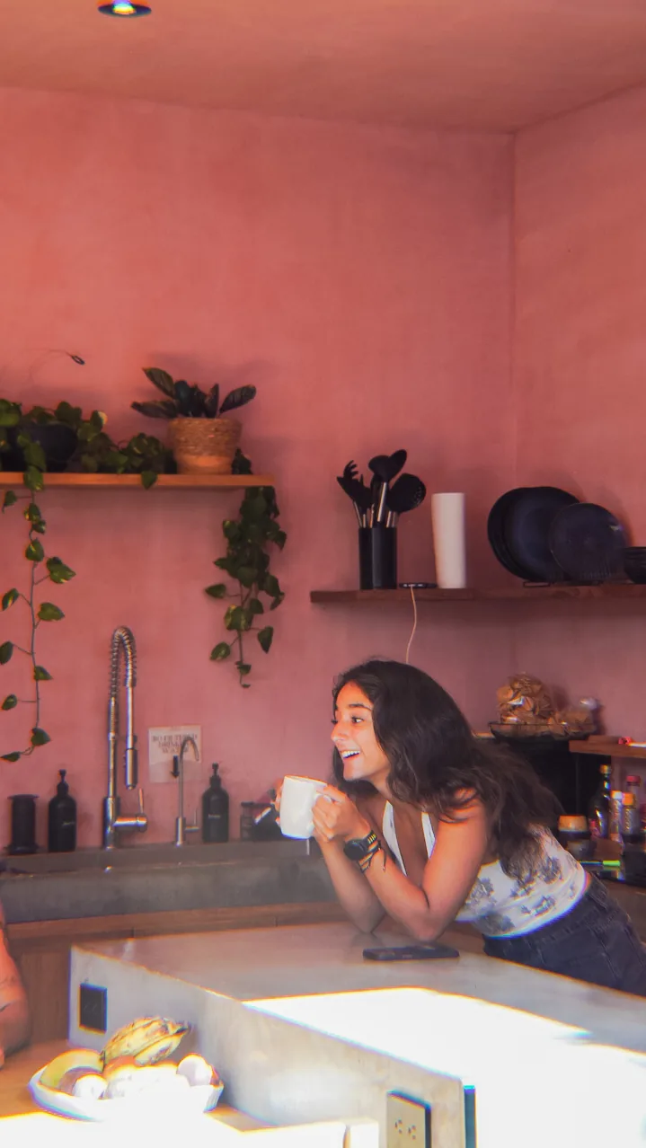 A guest laughing with a coffee mug at the counter of the plant-filled open-air kitchen at Amplitude Coliving, La Punta