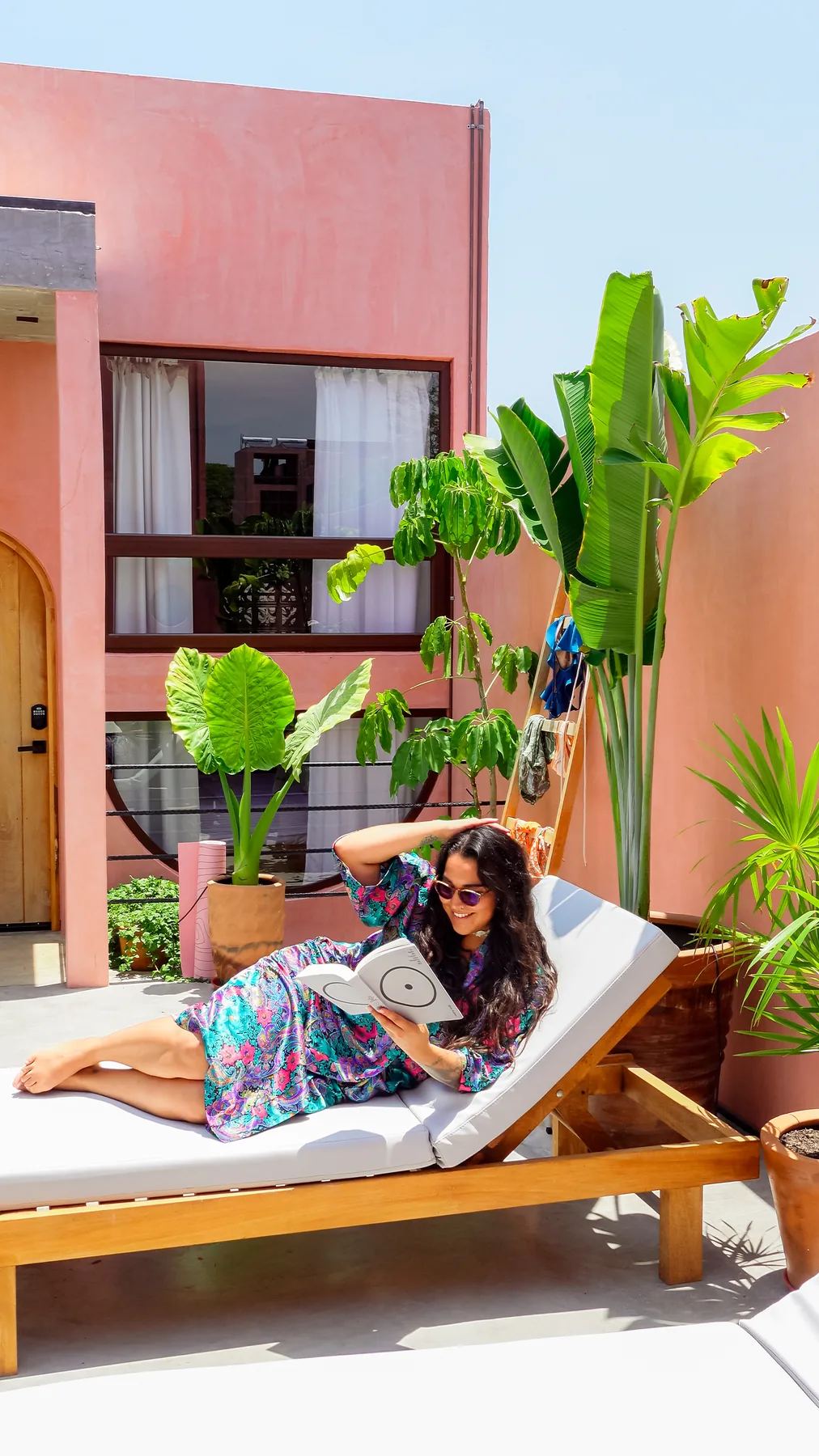 A guest reading on a sun lounger surrounded by tropical plants on the rooftop deck at Amplitude Coliving, La Punta